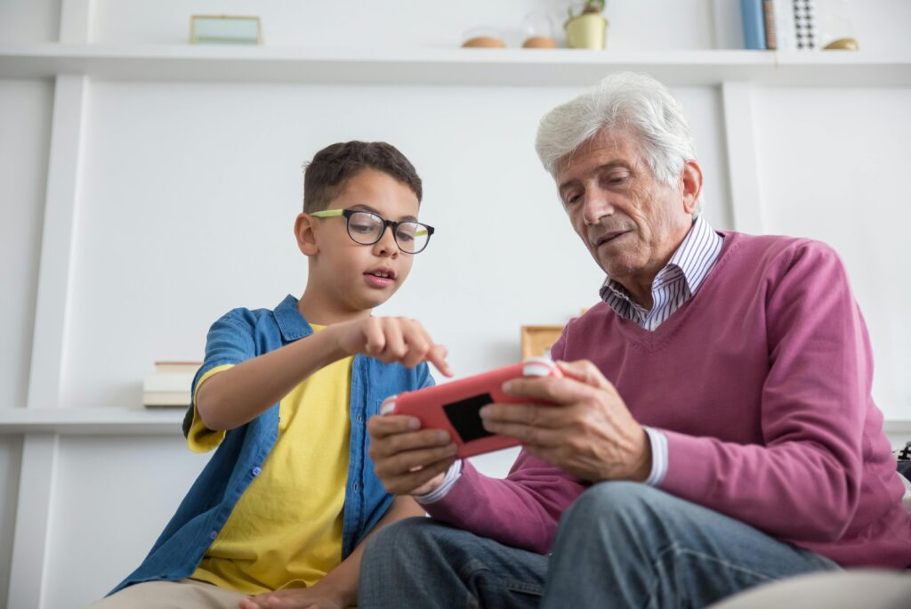 Senior man and young boy enjoying video games together indoors, fostering multi-generational connection.